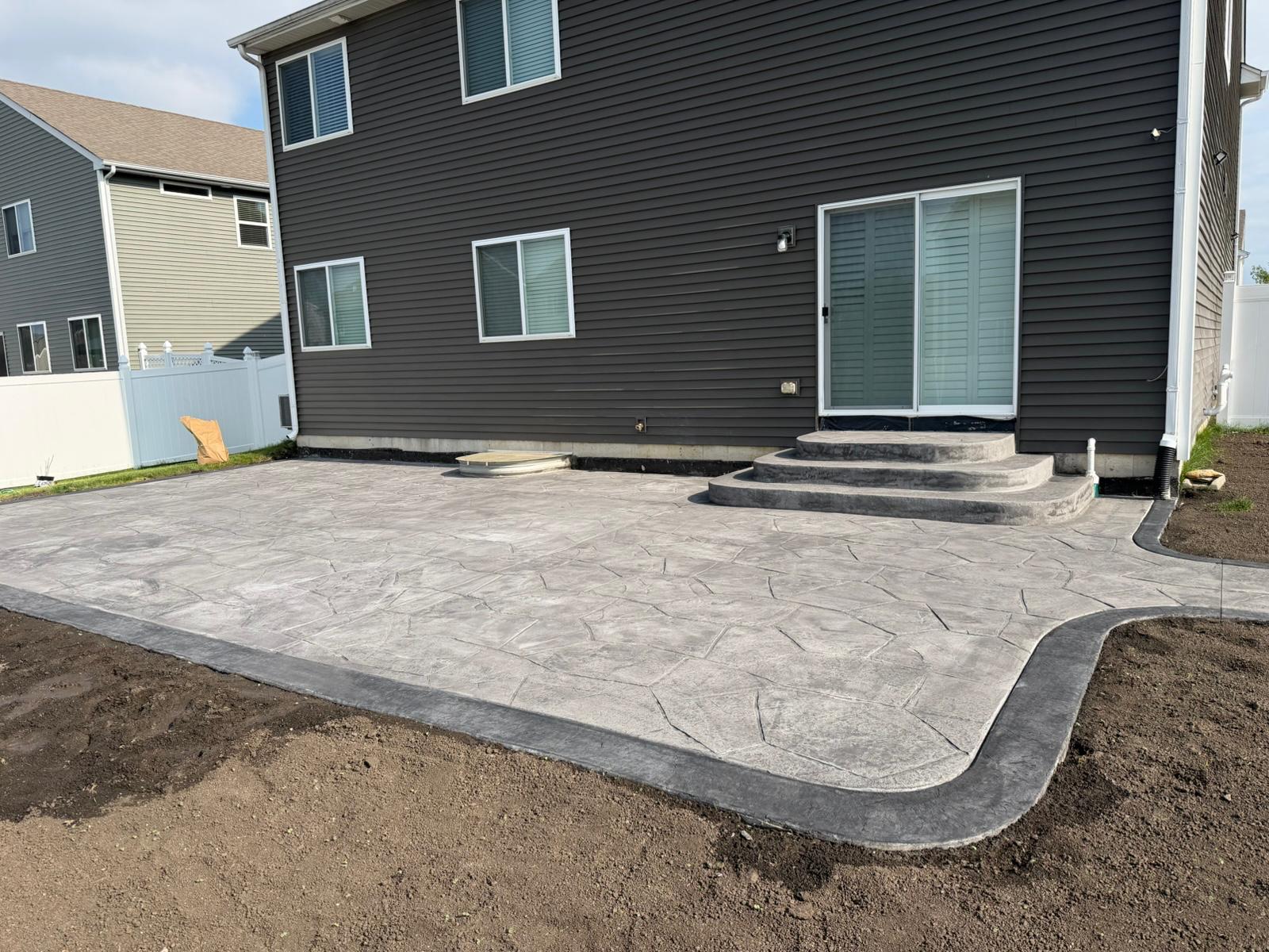 Freshly stamped concrete patio with curved border behind a home